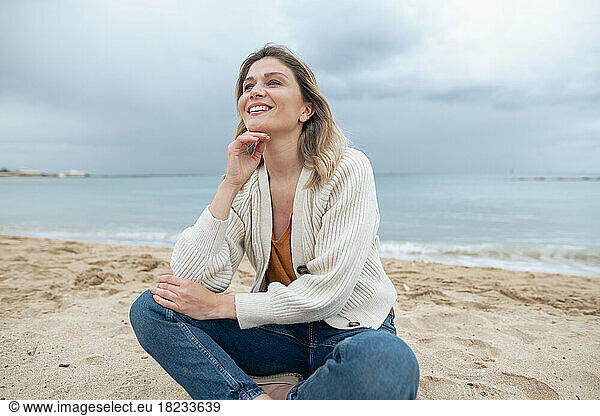 Smiling young beautiful woman sitting on sand day dreaming at beach
