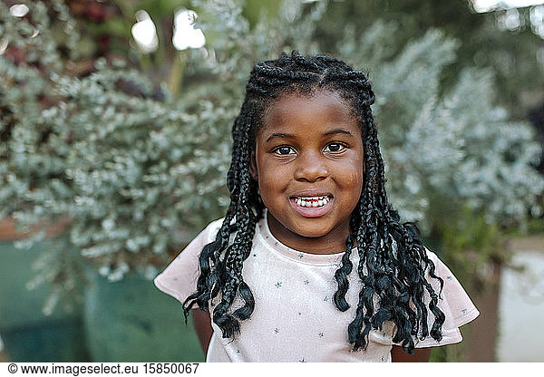 Smiling young black girl with long braids in front of potted plants