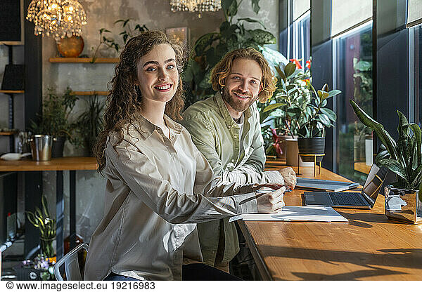 Smiling young business colleagues sitting at table in coffee shop