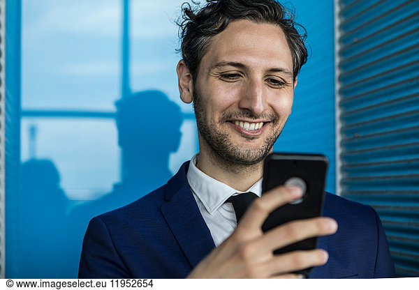 Smiling young businessman in city looking at smartphone