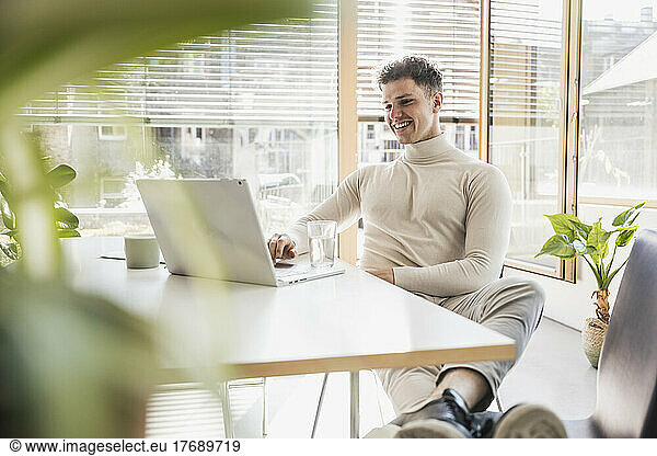 Smiling young businessman using laptop at desk in office