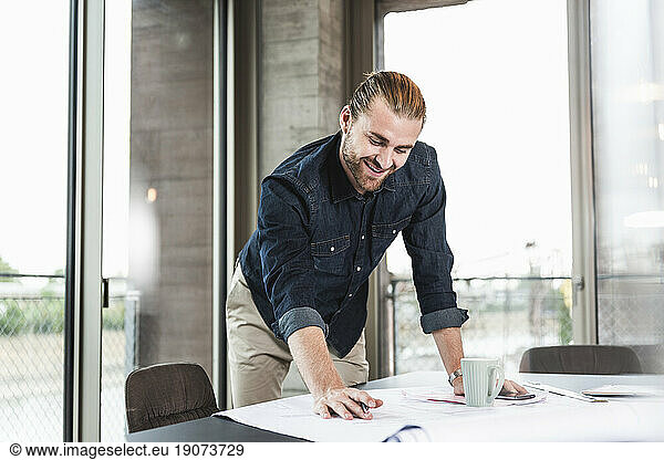 Smiling young businessman working on plan at desk in office