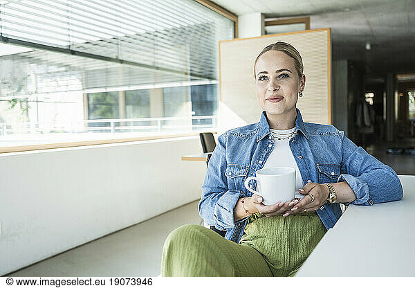 Smiling young businesswoman sitting with coffee cup at desk