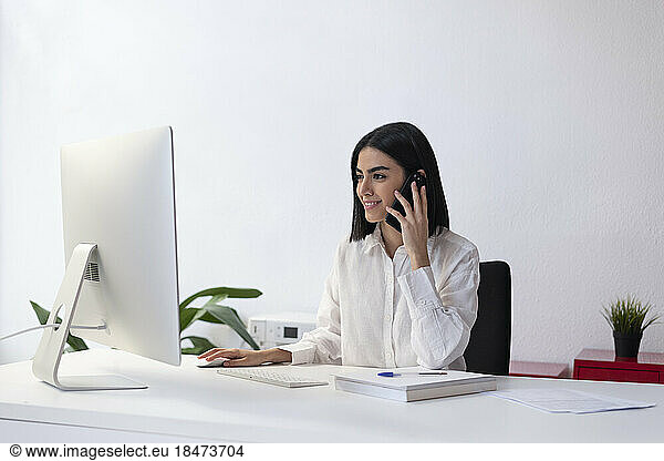 Smiling young businesswoman talking on smart phone at desk