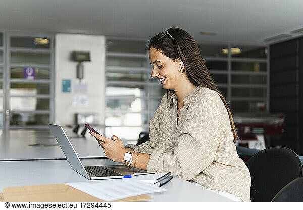 Smiling young businesswoman using smart phone at desk in office