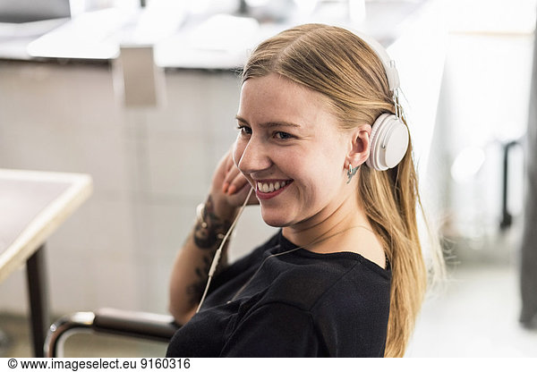 Smiling young businesswoman wearing headphones in creative office