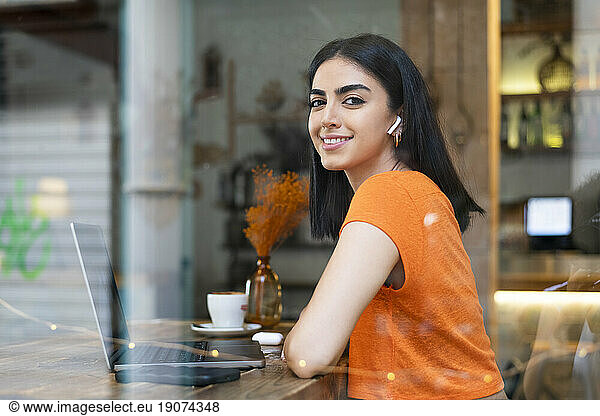 Smiling young businesswoman with laptop sitting in cafe