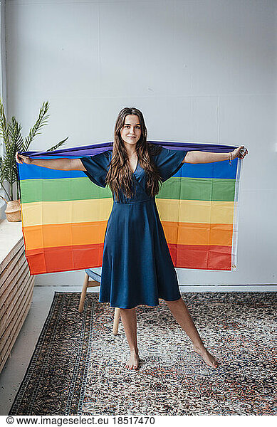 Smiling young businesswoman with rainbow flag standing in office