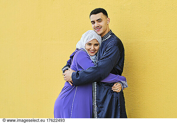 Smiling young couple embracing each other standing in front of yellow wall