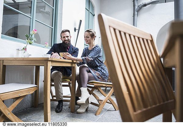 Smiling young couple using mobile phone at cafe