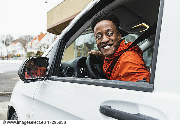 Smiling young driver looking back through window while driving delivery van
