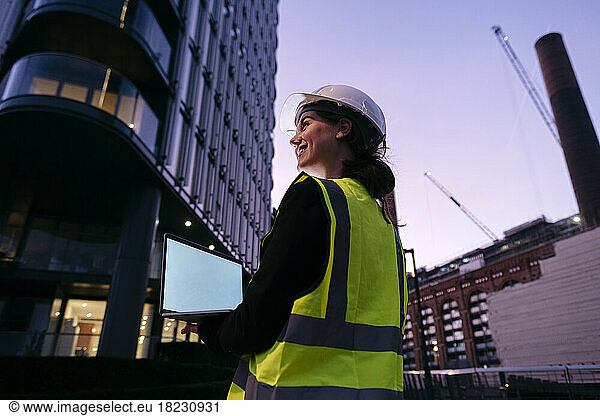 Smiling young engineer holding laptop at dusk