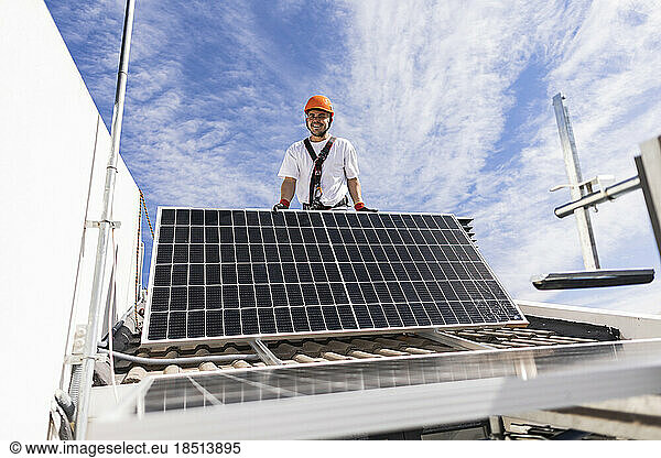 Smiling young engineer installing solar panels on roof