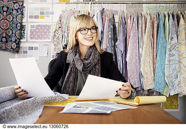 Smiling young female fashion designer working on desk in workshop