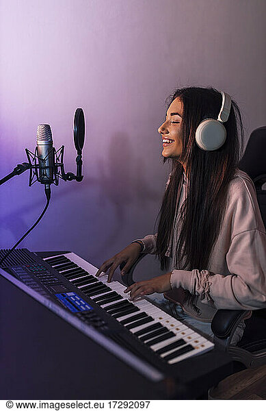 Smiling young female musician singing while playing piano at studio