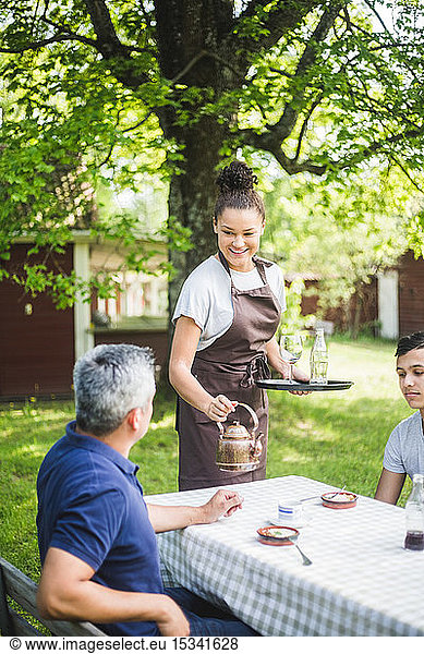 Smiling young female waitress serving drink for male customers sitting at outdoor cafe