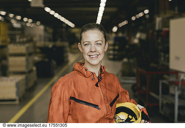 Smiling young female worker in orange protective workwear at factory