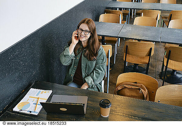Smiling young freelancer talking on smart phone in cafe