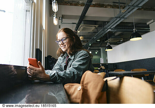 Smiling young freelancer using mobile phone in cafe
