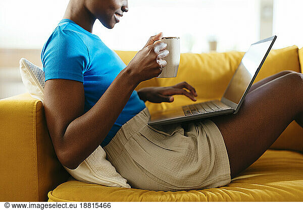 Smiling young freelancer with coffee cup working on laptop at home