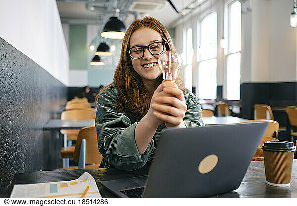 Smiling young freelancer with light bulb sitting in cafe
