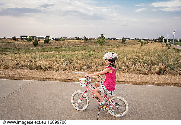 smiling young girl rides through a neighborhood park in the evening