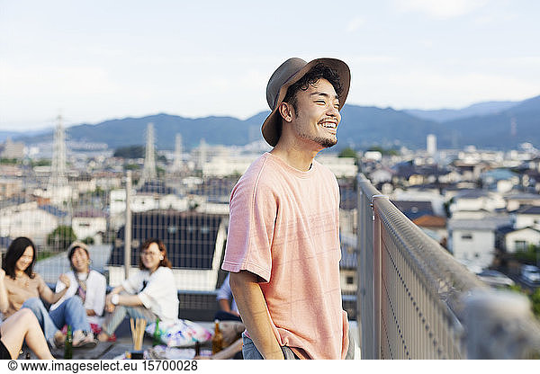 Smiling young Japanese man standing on a rooftop in an urban setting.