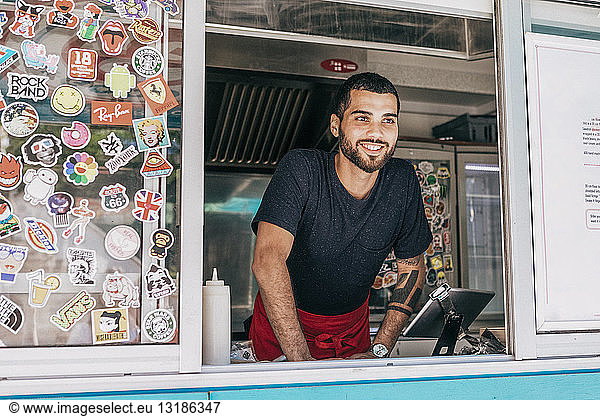 Smiling young male owner standing in food truck seen through window