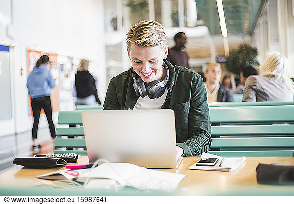 Smiling young male student using laptop in cafeteria at university