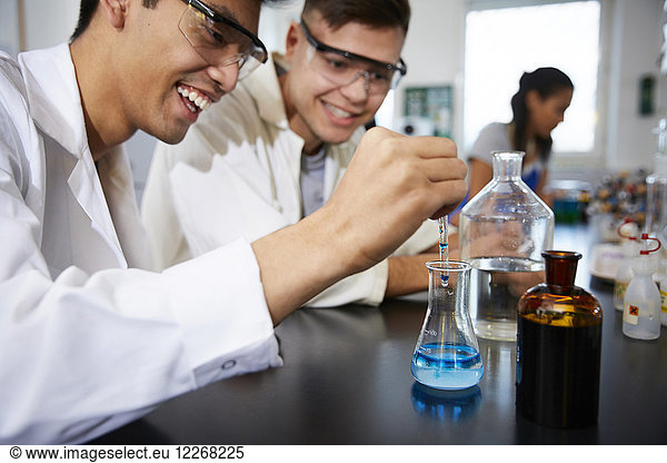 Smiling young male students mixing solutions in glassware at chemistry laboratory