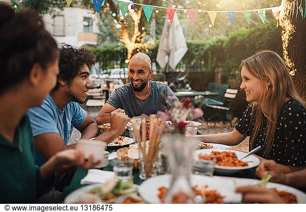 Smiling young man and women listening to male friend talking during dinner party in backyard