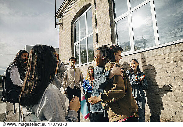 Smiling young man embracing woman by friends outside building
