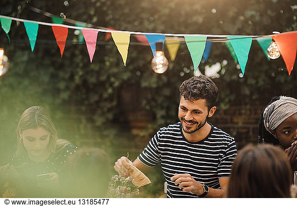 Smiling young man enjoying dinner party with friends in backyard