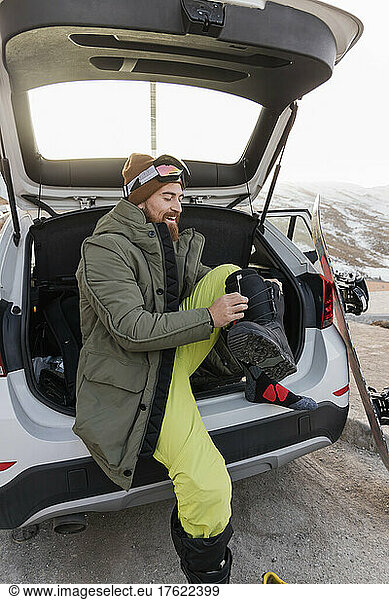 Smiling young man in car trunk preparing for snowboarding