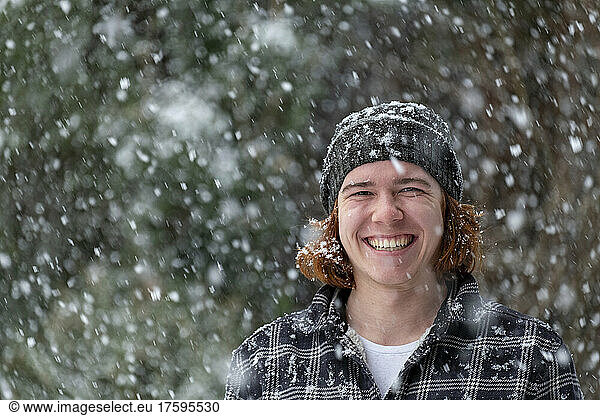 Smiling young man in knit hat enjoying snowfall
