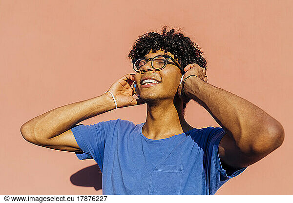 Smiling young man listening music through headphones on sunny day