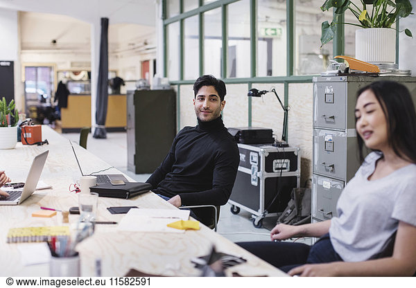 Smiling young man looking at female colleague in creative office