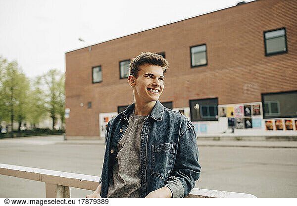 Smiling young man looking away while leaning on railing