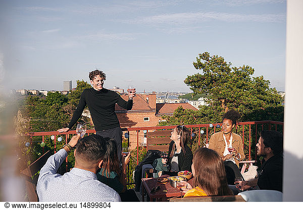 Smiling young man raising toast during social gathering on terrace
