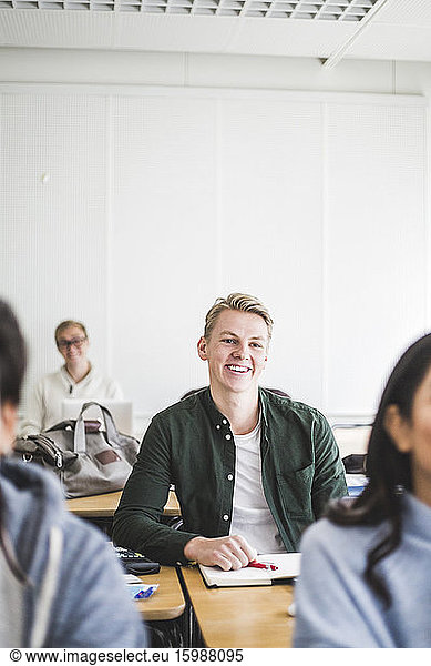 Smiling young man sitting at desk in classroom