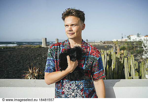Smiling young man standing with black dog on sunny day