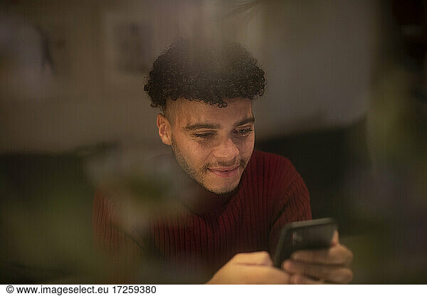Smiling young man using smart phone in window