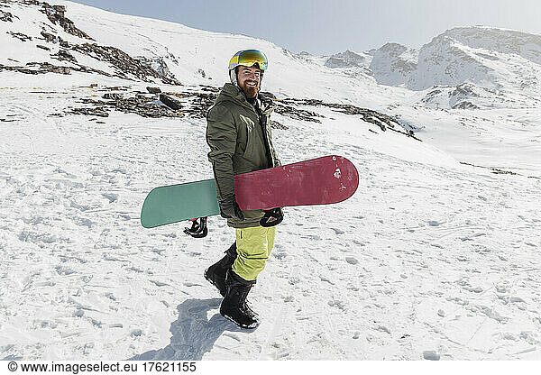 Smiling young man walking with snowboard on sunny day