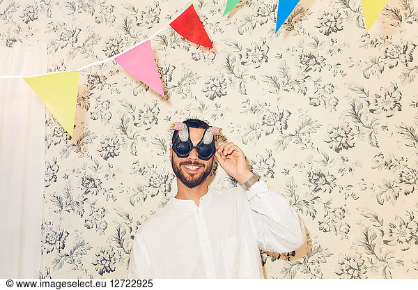Smiling young man wearing eyewear while standing against wallpaper at apartment during party
