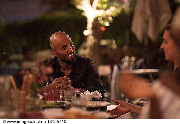 Smiling young man with shaved head looking at female friend while sitting at table during dinner party