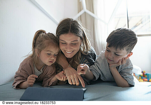 Smiling young mother with children using tablet PC in bedroom at home