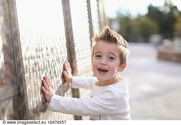 Smiling young preschooler boy touching a metal wall.