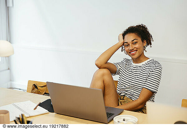 Smiling young student with laptop sitting at desk