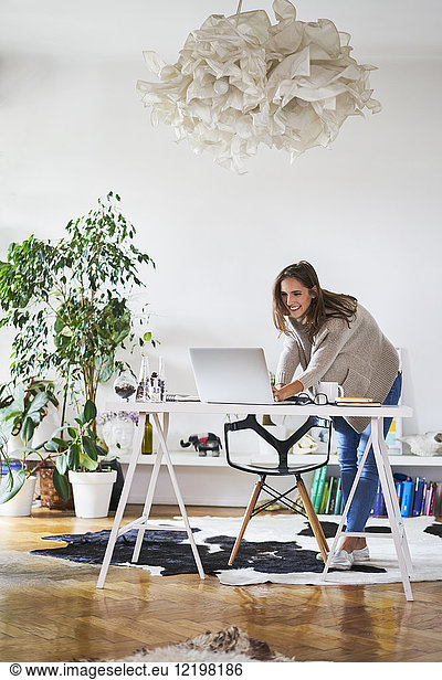Smiling young woman at home using laptop on desk