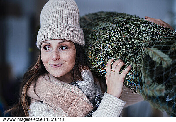 Smiling young woman carrying Christmas tree